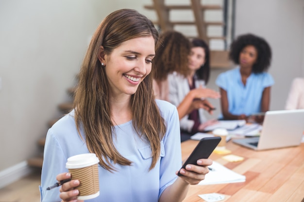 Donna di affari che per mezzo del telefono cellulare mentre mangiando caffè