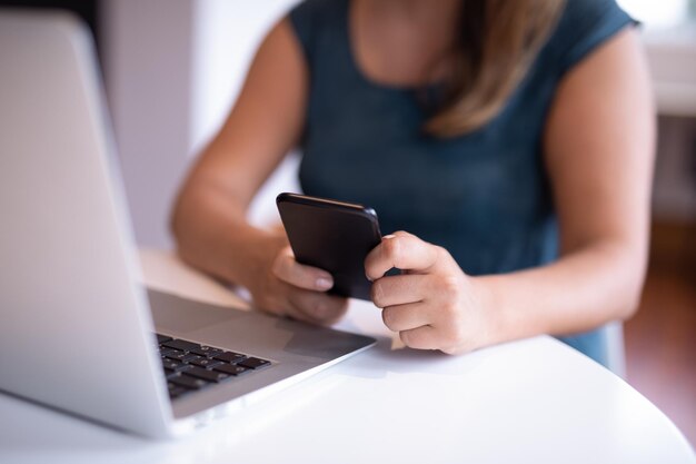 Businesswoman using mobile phone while working on laptop in a modern office