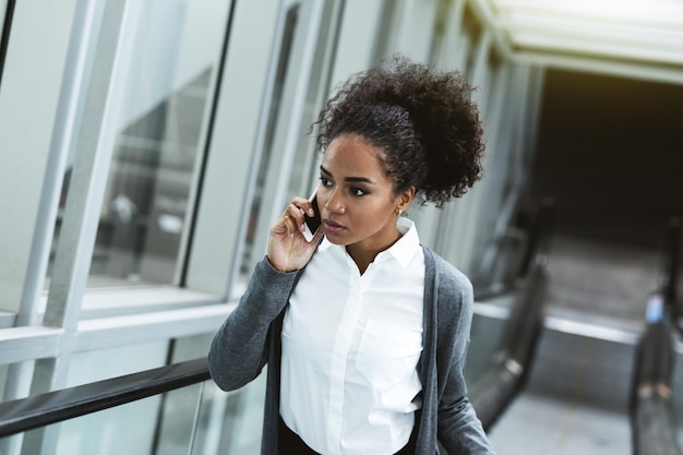 businesswoman using phone while standing on escalator