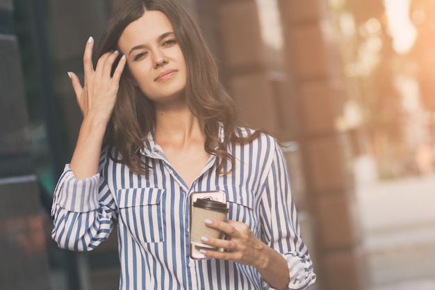 彼女の手にコーヒーを飲みながら街の通りを歩いている実業家。