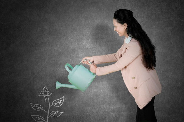 Businesswoman water a drawn plant on blackboard