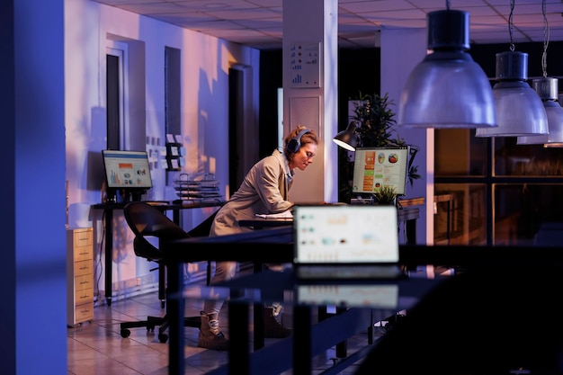 Businesswoman wearing headphones analyzing financial growth report in startup office. Executive manager listening music and having fun after finishing company strategy. Corporate concept