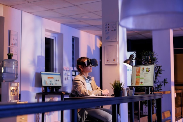 Businesswoman wearing virtual reality headset in startup office, analyzing financial growth report. Executive manager working overtime at company strategy using vr goggles. Technology concept