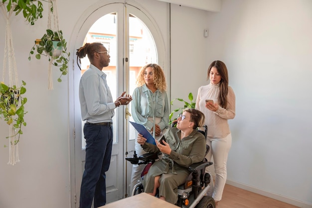 A a businesswoman in a wheelchair with a disability discuss business strategy with her multiracial colleagues near to the window