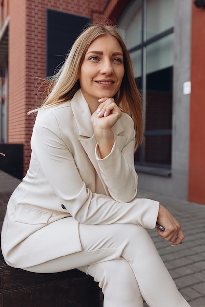 businesswoman in white elegant suit looking forward with aspiration while sitting near contemporary