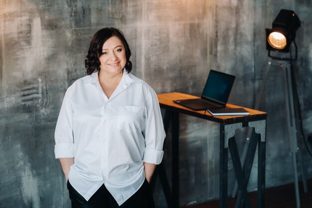 A businesswoman in a white shirt and pants stands in her office.