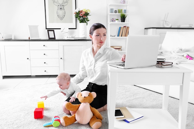 Businesswoman with baby boy on carpet working from home using laptop