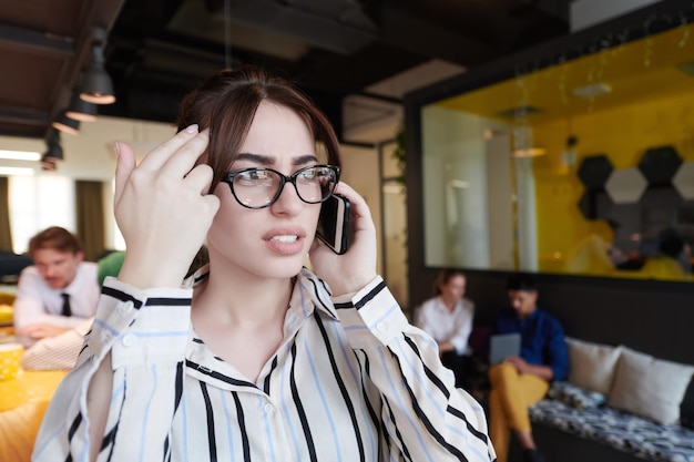 Деловая женщина в очках с мобильным телефоном в современном стартапе открытого плана офисного интерьера