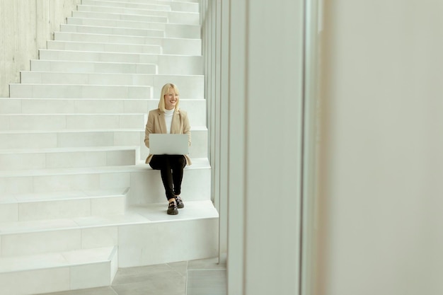 Businesswoman with laptop on modern office stairs