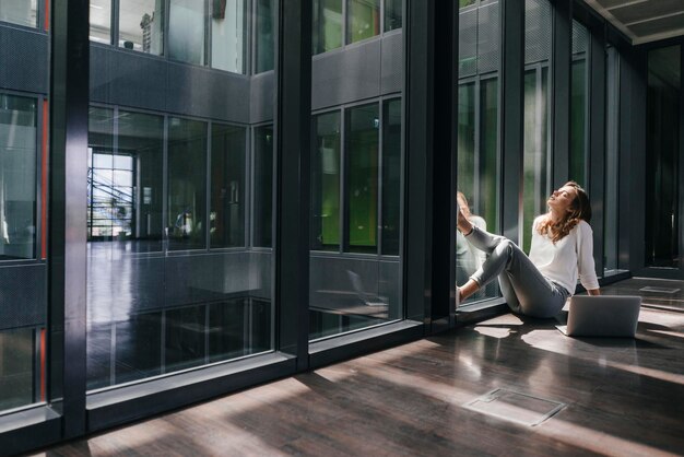 Photo businesswoman with laptop, sitting on floor, daydreaming