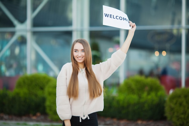 Businesswoman with long Hair Holding a sign Board with a Welcome has Airport