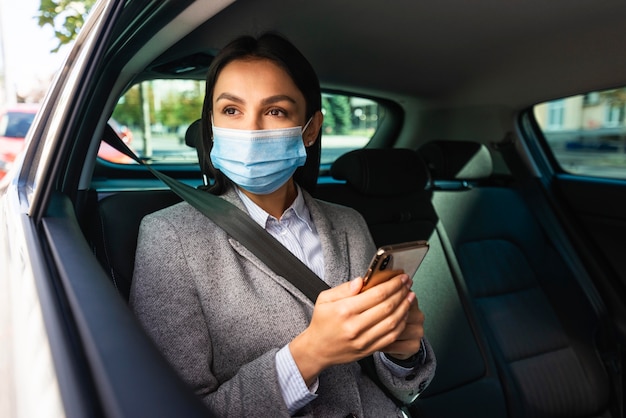 Businesswoman with medical mask and smartphone in the car