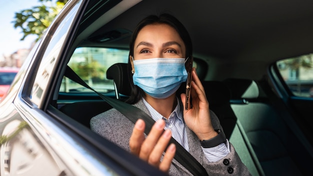 Businesswoman with medical mask talking on the phone in car