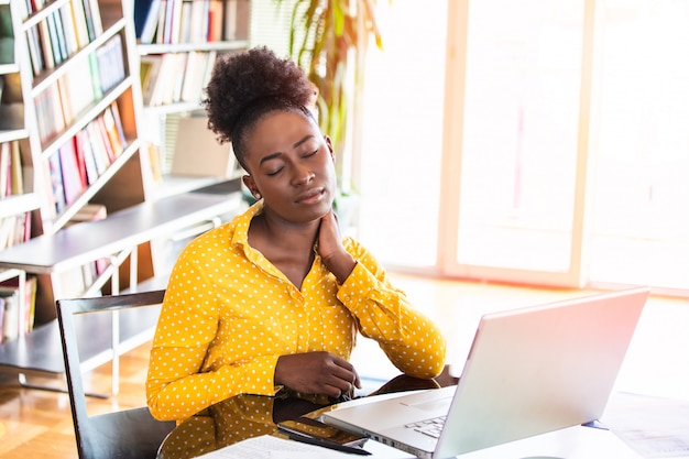 Businesswoman with a neck pain sitting at the table with laptop