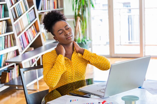 Businesswoman with a neck pain sitting at the table with laptop