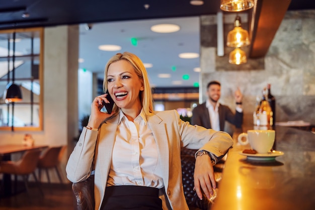 A businesswoman with positive energy sits in a cafe for a coffee break and makes a phone call. Telecommunications, free time, break, social networks