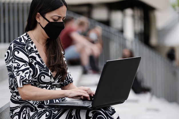Деловая женщина с защитной маской, работающая со своим ноутбуком на улице