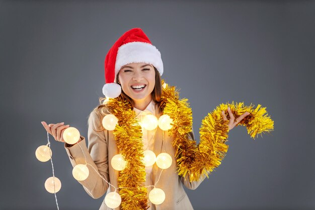 Imprenditrice con cappello di babbo natale sulla testa, con decorazioni natalizie intorno al collo che celebrano