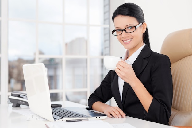 Businesswoman at work. Confident young business woman sitting at her working place and drinking coffee