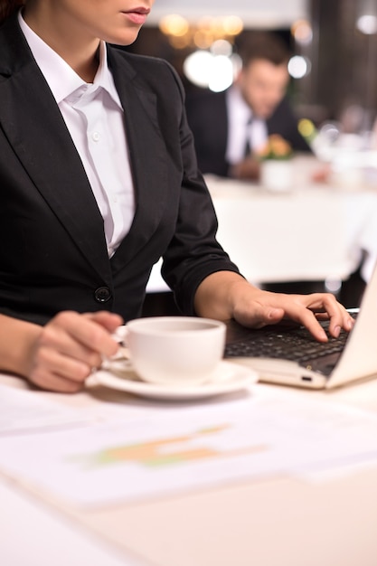 Businesswoman at work. Cropped Image of young woman in formalwear working on laptop and holding a coffee cup while sitting at the restaurant