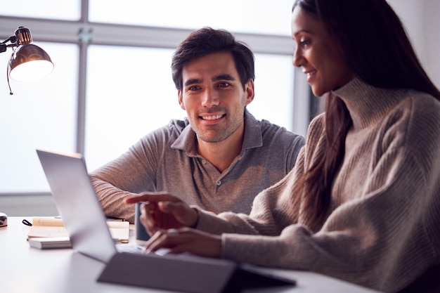 Businesswoman Working On Laptop At Desk Collaborating With Male Colleague