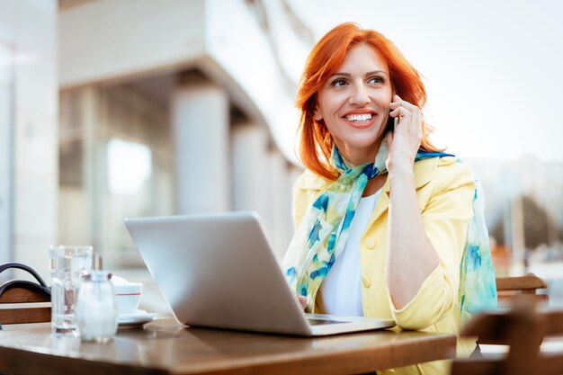 Businesswoman working at the laptop and using phone on a coffee break in a street cafe.