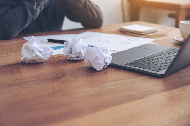 失敗のように感じて働いていて、オフィスのテーブルの上でめちゃくちゃな紙とラップトップでストレスを感じている実業家