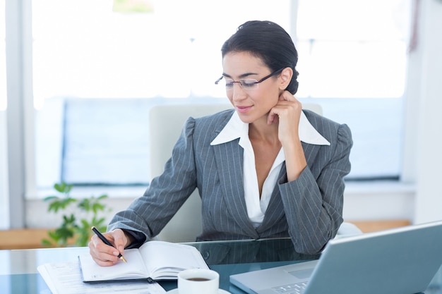 Businesswoman working with her laptop and writing notes