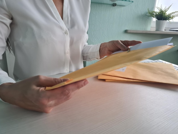 Businesswoman in workplace opens yellow envelope and takes out sheet of notification of received paper letter