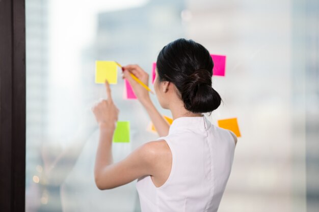 Photo businesswoman write notes on the paper attached to the window glass