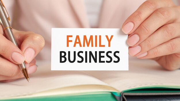 Businesswoman writes in a notebook with a silver pen and hand hold card with text: FAMILY BUSINESS