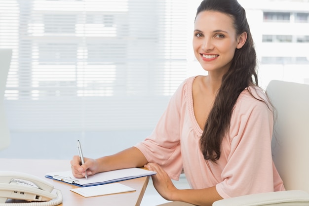 Businesswoman writing on clipboard at a bright office