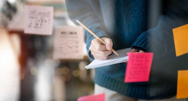 Foto donna d'affari che scrive nota e utilizza post-it nel piano aziendale di strategia della parete di vetro per lo sviluppo crescere fino al successo