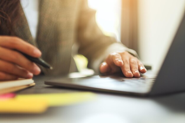 Businesswoman writing on paperwork while typing on laptop computer on the table in office