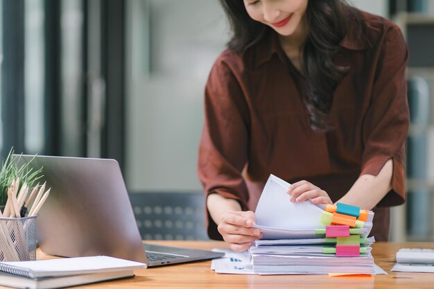 Photo the businesswomans hands are busy working amidst stacks of paper files searching and checking for unfinished documents among the folders and papers on her cluttered office desk