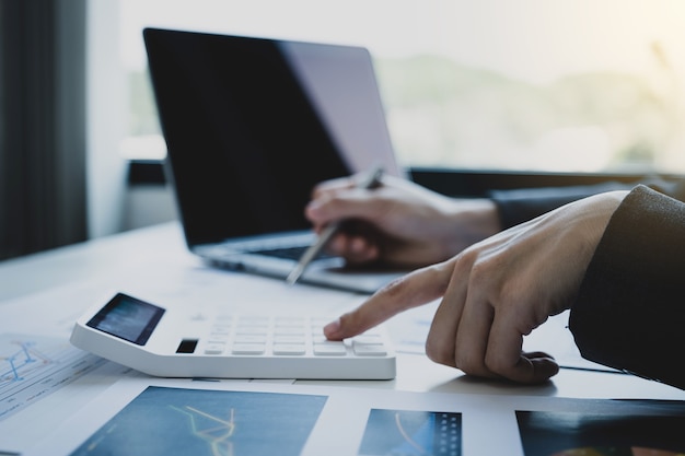 Businesswomen bookkeeper holds calculator and laptop on white desk in working office