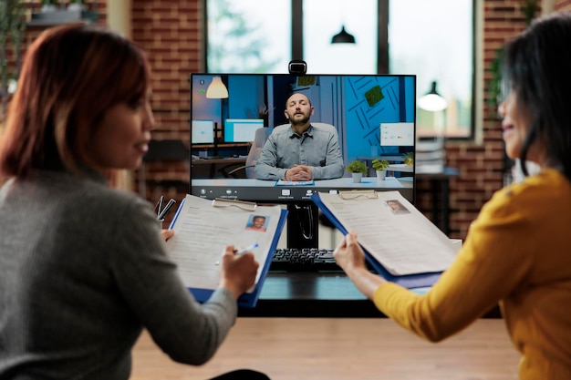 Photo businesswomen holding clipboard analyzing freelancers cv discussing company hiring plan with applicant during online videocall meeting conference in startup office. teleconference call