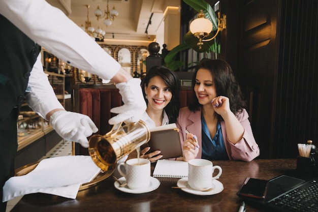 ビジネスウーマンはカフェに座ってコーヒーを飲み、ビジネス会話をしてビジネスについて話し合い、楽しんでいます