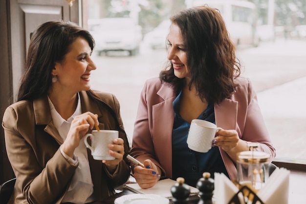 Businesswomen sit in a cafe drink coffee and have a business\
conversation discuss business and have fun
