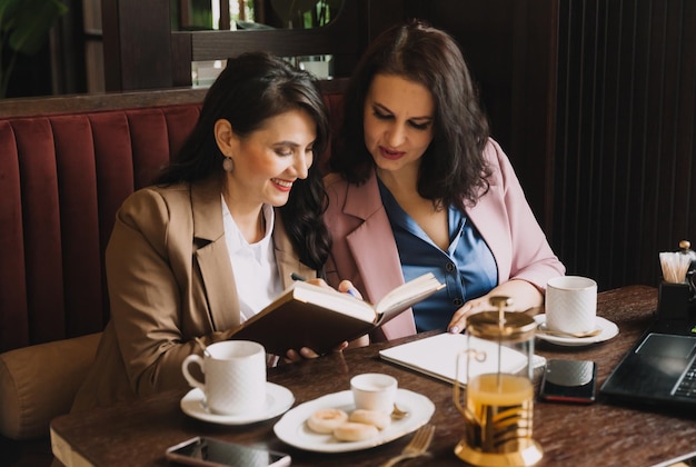 Businesswomen sit in a cafe drink coffee and have a business\
conversation discuss business and have fun