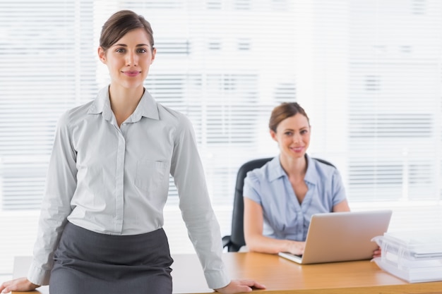 Businesswomen smiling at camera with one sitting and one standing