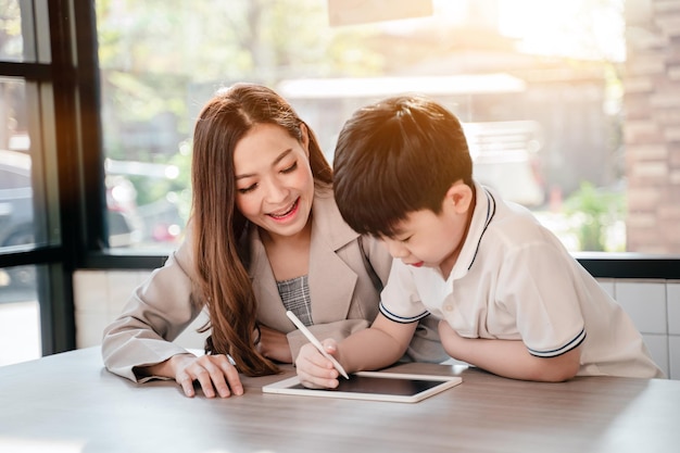 子供と一緒にカフェでオンラインで働くビジネスの女性。携帯電話とデジタルタブレットでアジアの家族のライフスタイル。