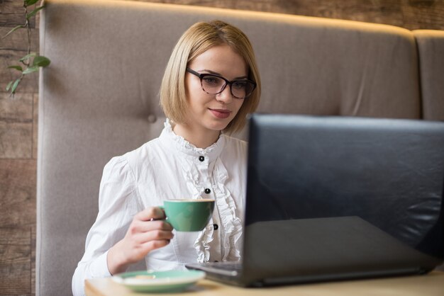 カフェでノートパソコンを使用して忙しい女性。コーヒーショップに座って、コンピューターで作業している若い美しい少女