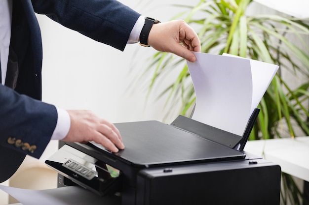 Bussinessman laadt papier met de hand naar de printerscanner of laserkopieermachine op kantoor