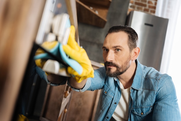 Busy appealing male cleaner working and wiping fingerprints while putting on gloves