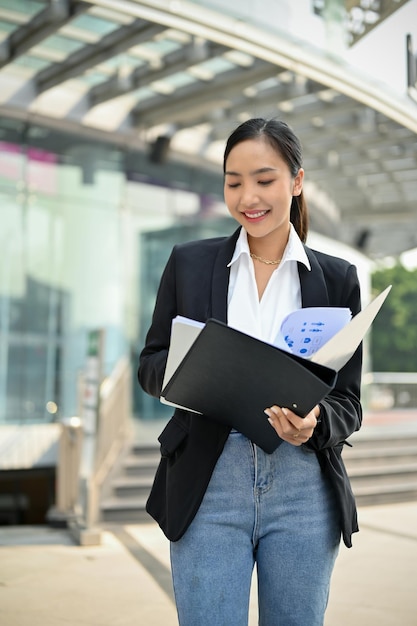 Busy Asian female CEO checks a financial report in a document file outside of the company building