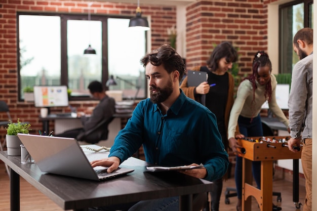 Busy businessman analyzing marketing statistics working at business project in brick wall startup office. Freelancer man typing company turnover on laptop computer brainstorming ideas