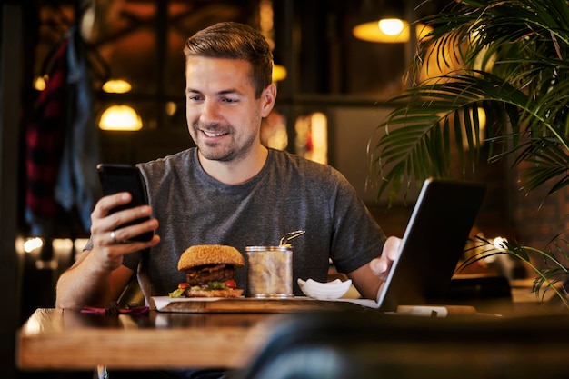 A busy casual man is sitting in restaurant on a lunch break and using technologies for business