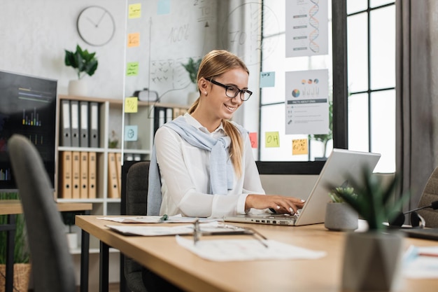 Busy caucasian woman in white shirt sitting at office and using wireless laptop