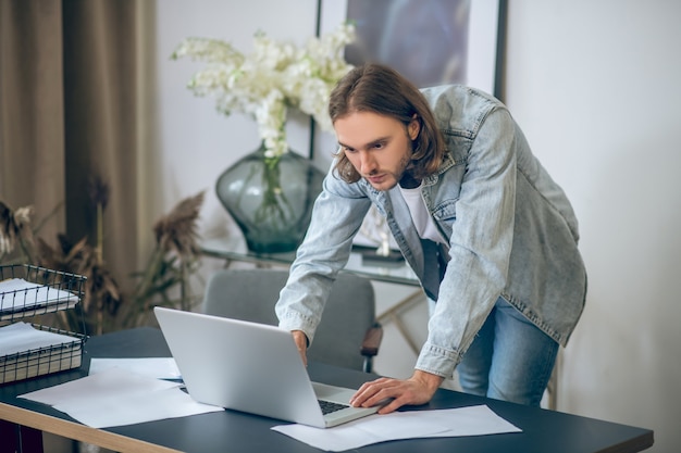 Busy day. Man in jeans shirt working on laptop and looking busy